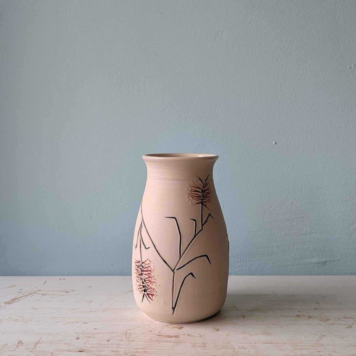 Ceramic vase with floral bottlebrush design on a white table against a blue wall.