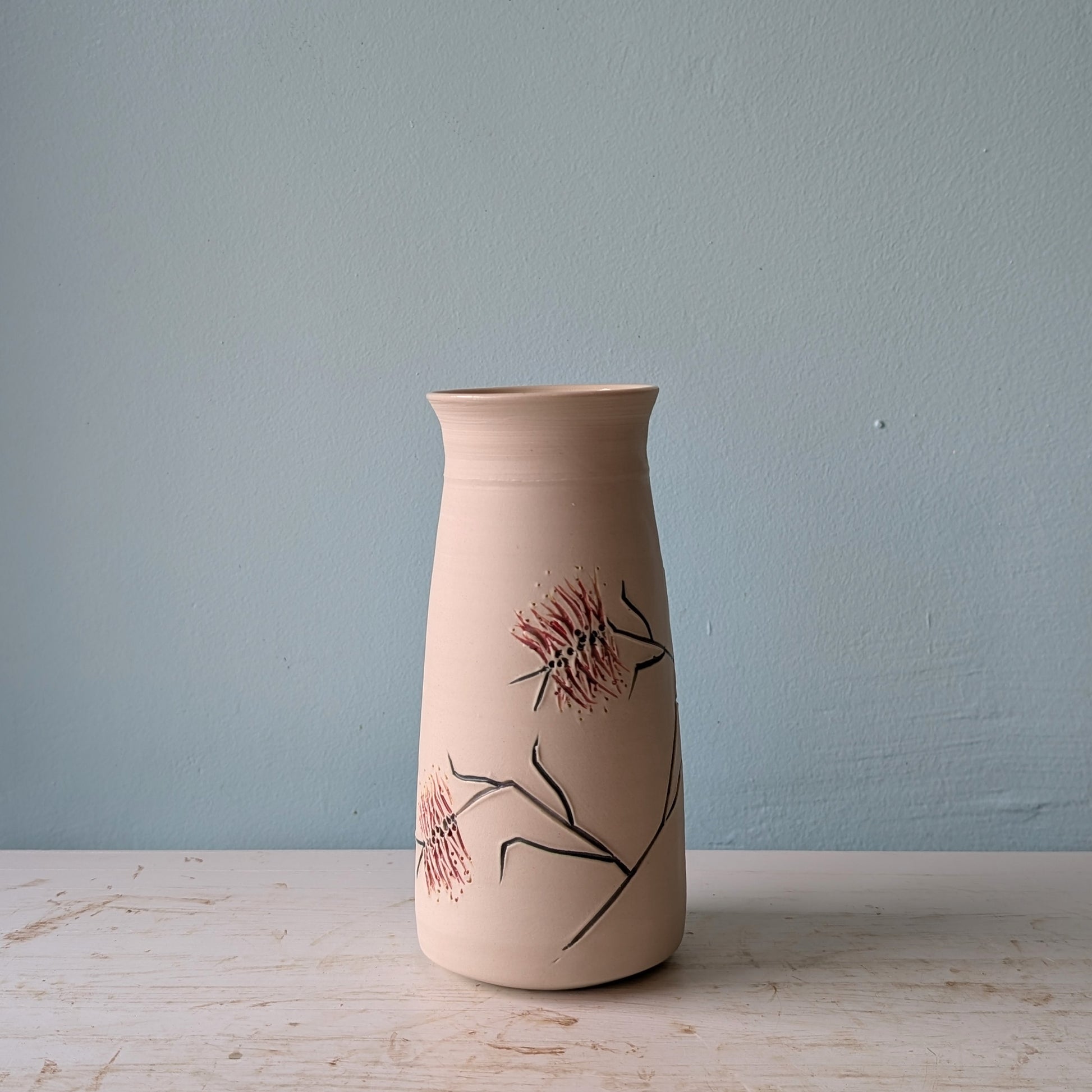 Ceramic vase with floral bottlebrush design on a white table against a blue wall.