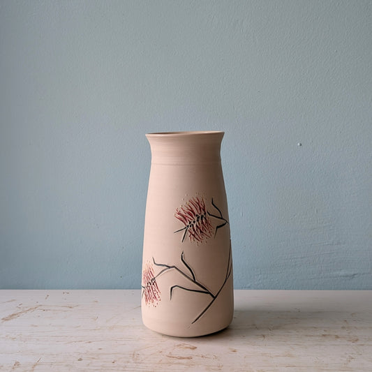 Ceramic vase with floral bottlebrush design on a white table against a blue wall.