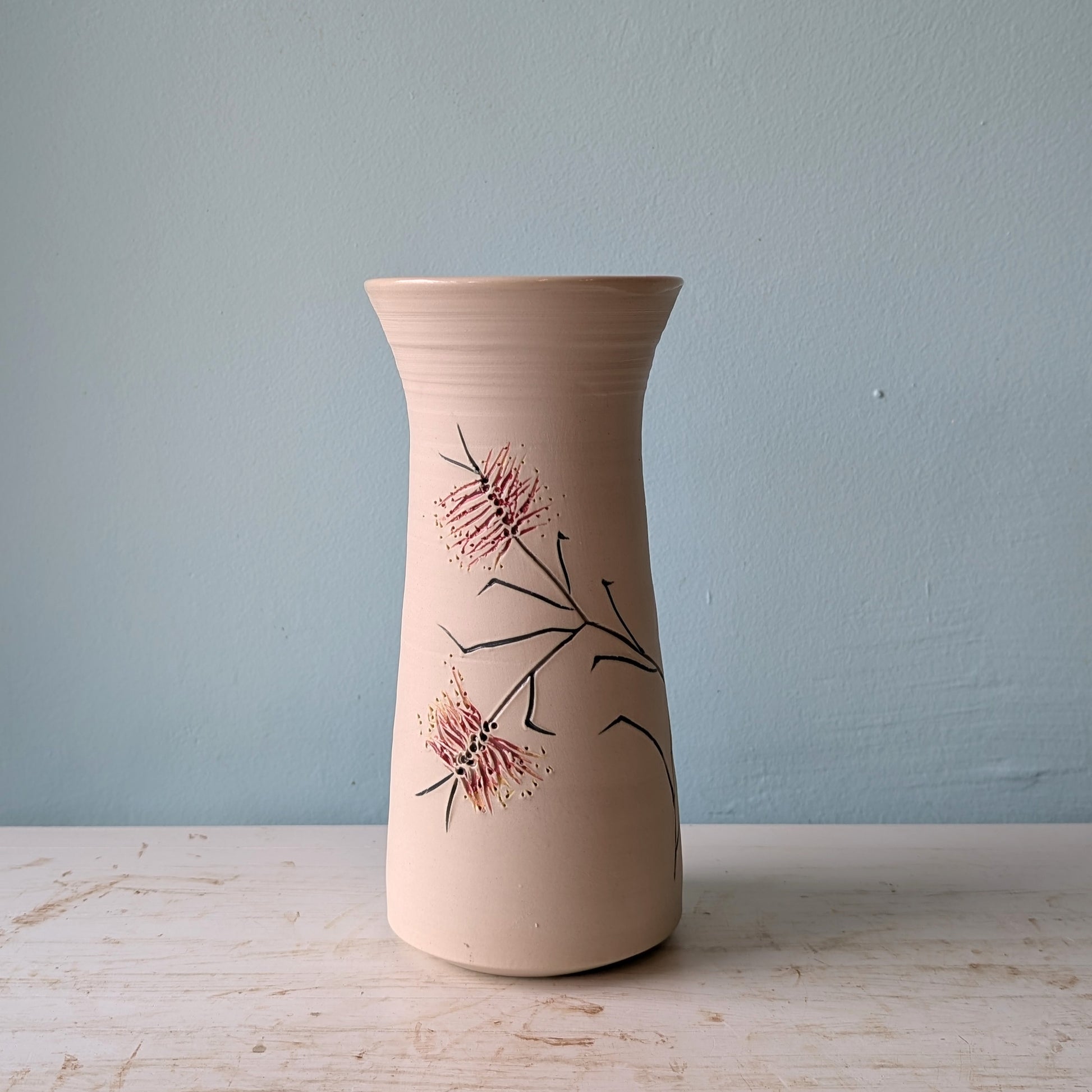 Ceramic vase with floral bottlebrush design on a white table against a blue wall.