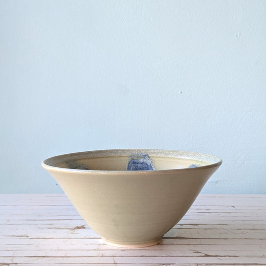 Front view of a beige serving bowl with blue brushstroke pattern interior, on a white table with blue background.