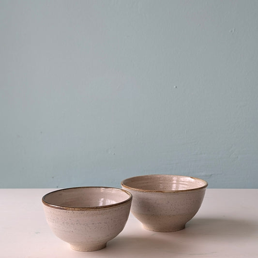 Two beige ceramic bowls on a white table against a blue background