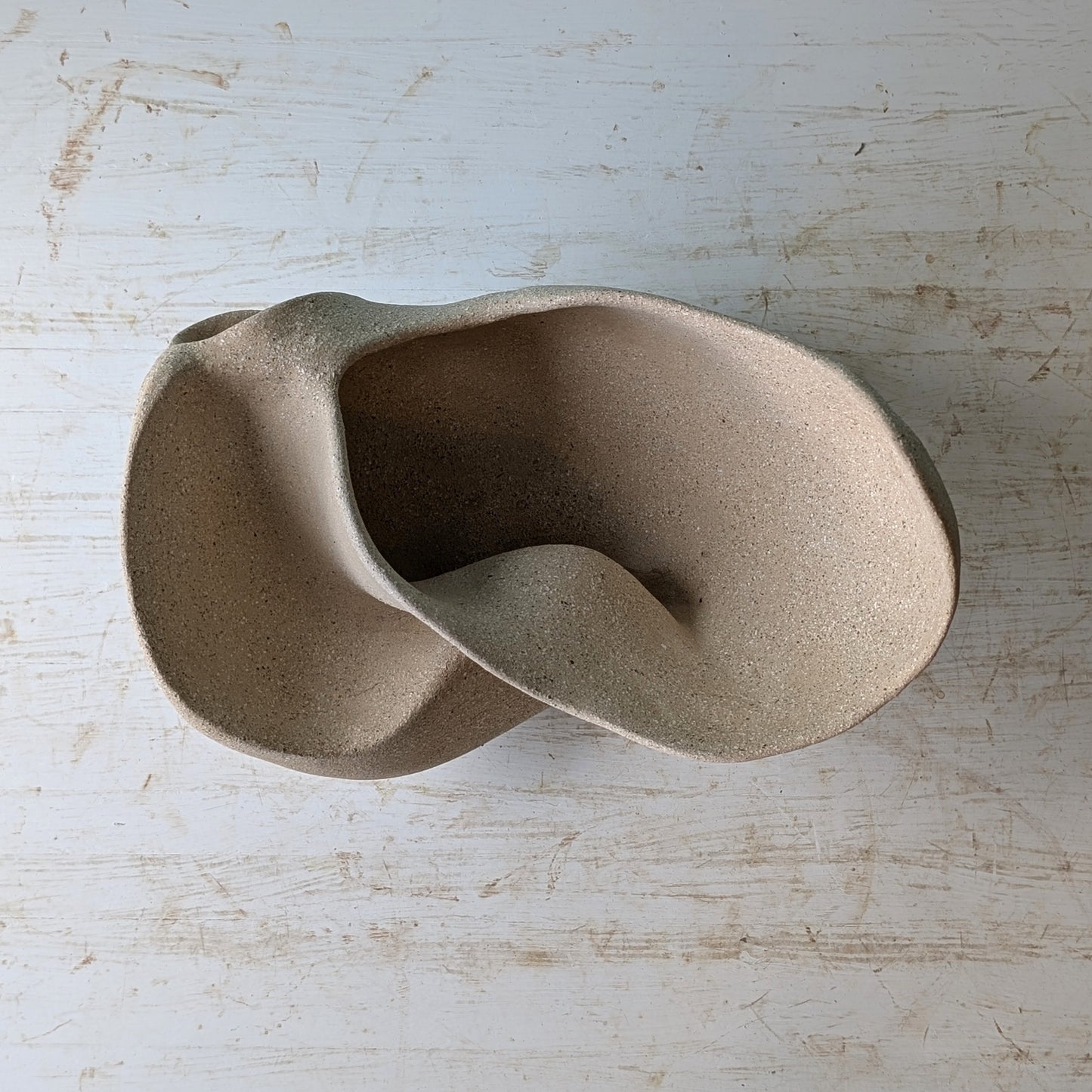 Sculptural bowl made of beige matte ceramic on a white table against a blue wall.