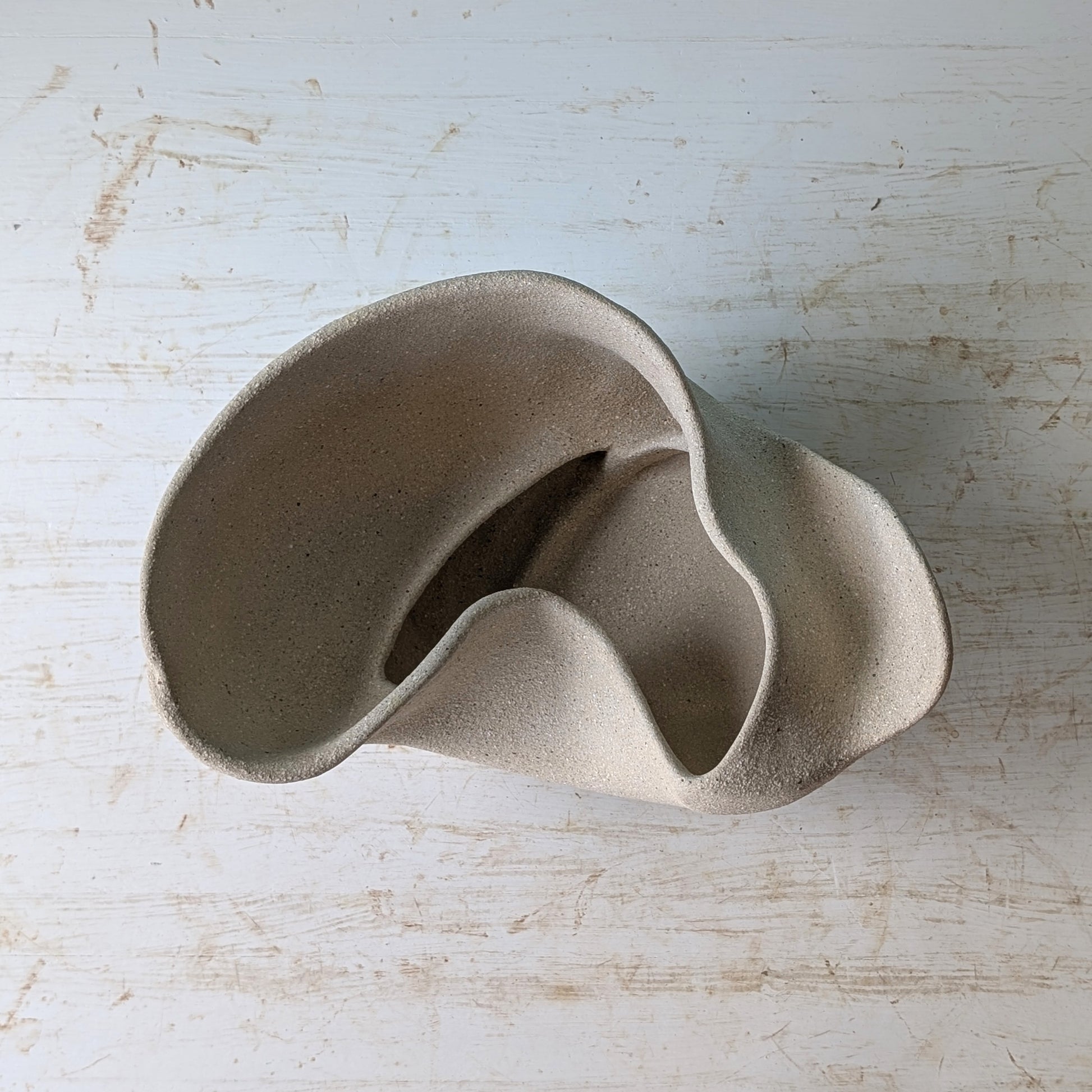 Sculptural bowl made of beige matte ceramic on a white table against a blue wall.