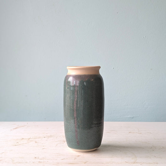 Green ceramic vase on a white table against a blue wall