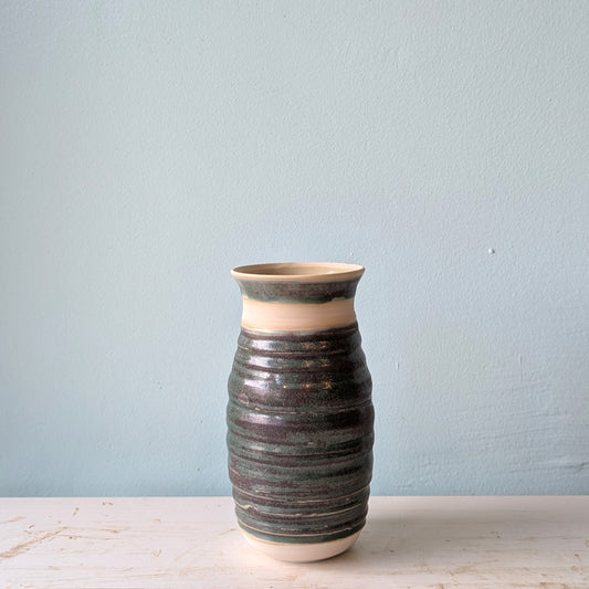 Bottle green ceramic vase on a white table against a blue wall.