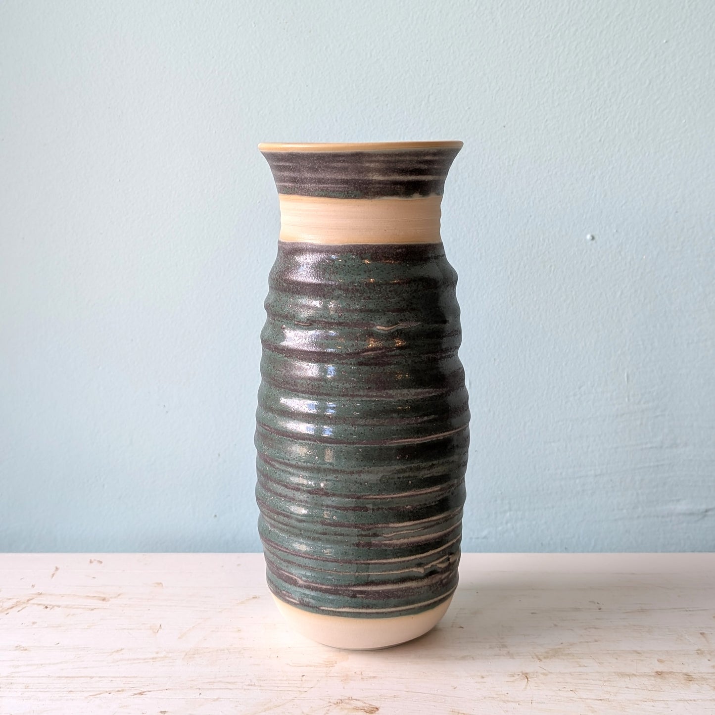 Forest green ceramic vase on a white table against a blue wall.