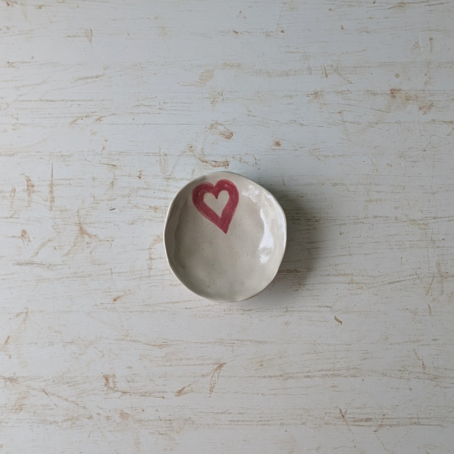 Small white ceramic dish with a pink heart on a light wooden surface
