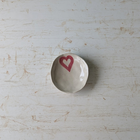 Small white ceramic dish with a pink heart on a light wooden surface