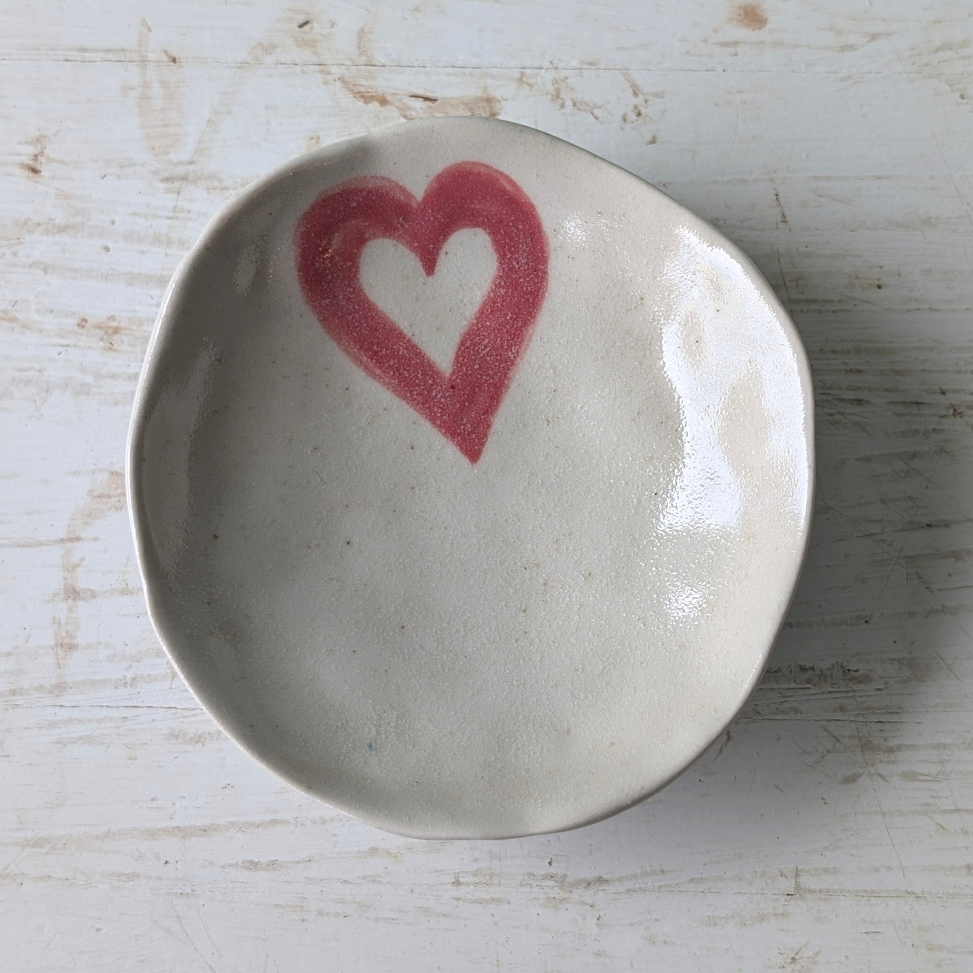 Small ceramic dish with a pink heart design on a light wooden surface