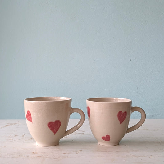 Two pink mugs with pink heart designs on a light blue background