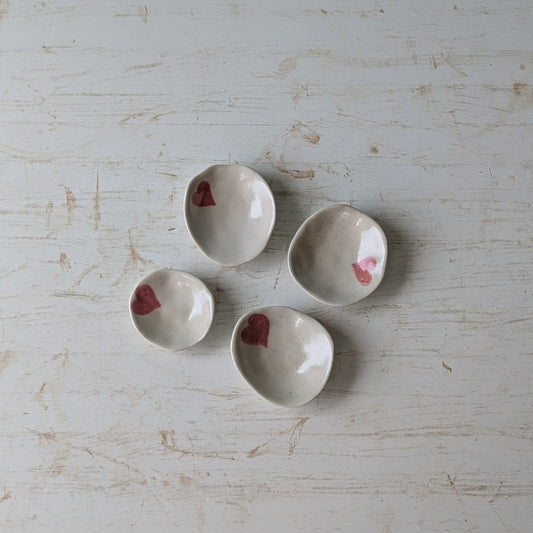 Four small ceramic bowls with pink heart designs on a textured light background