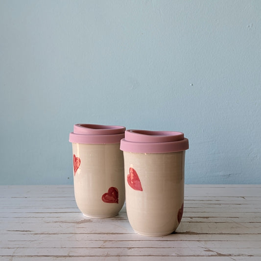 Two reusable ceramic takeaway cups with silicon lids and pink heart pattern