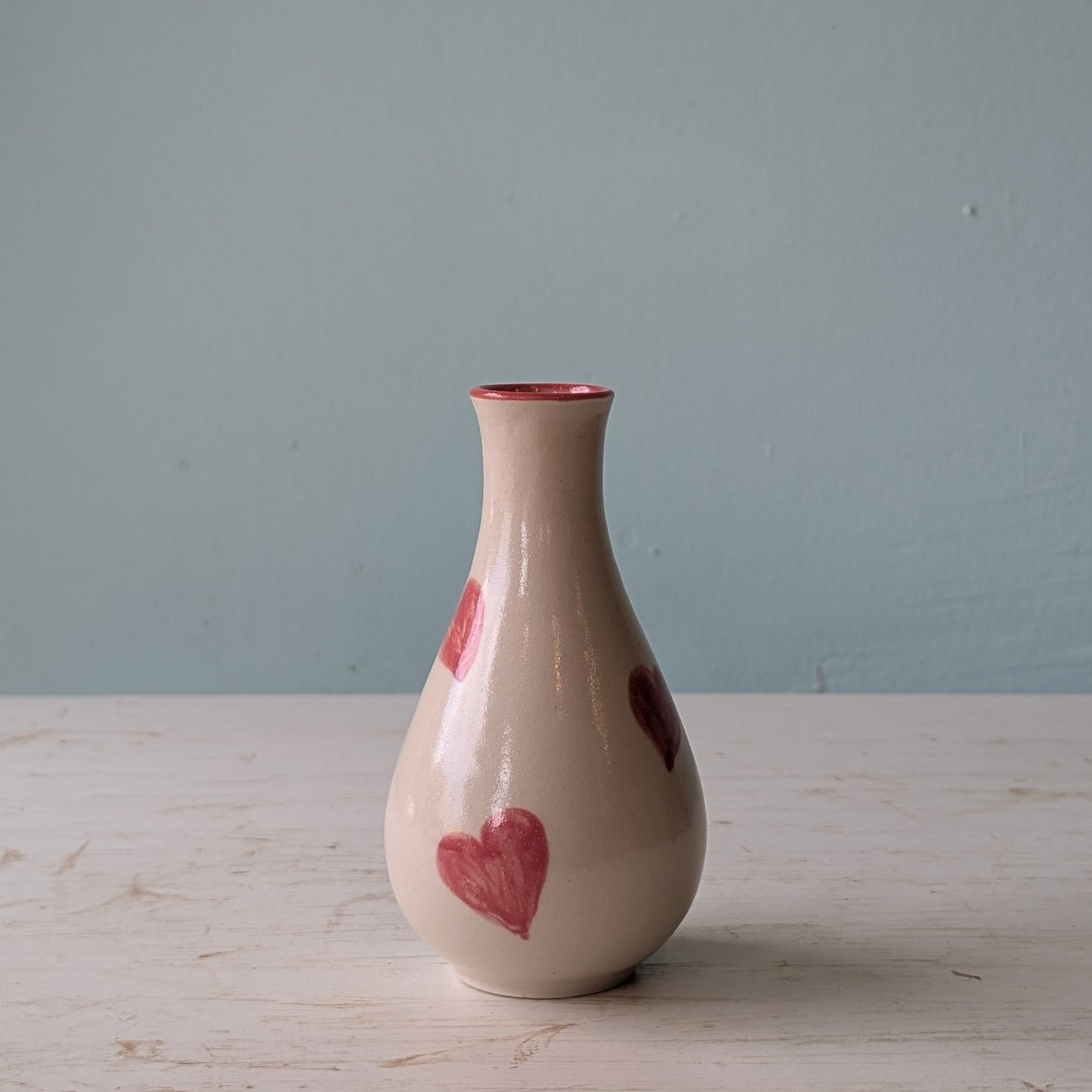 Ceramic vase with pink heart designs on a wooden surface and light blue background