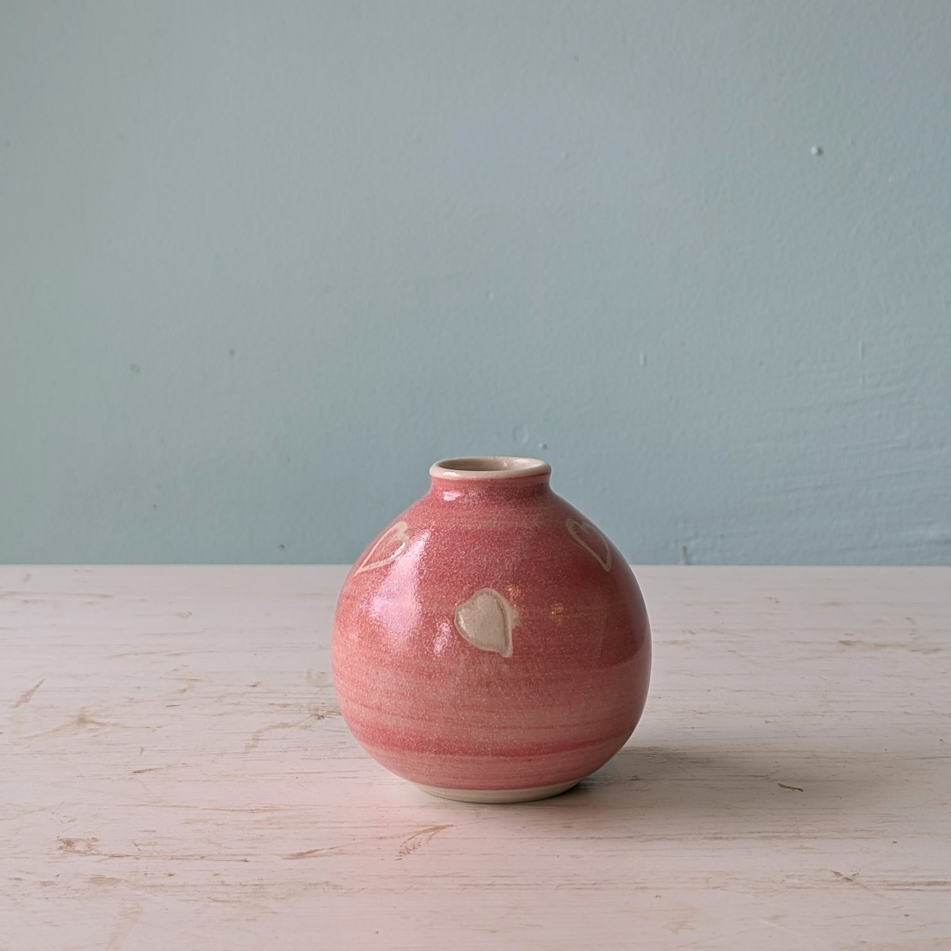 Pink ceramic vase on a wooden surface with a light blue wall background