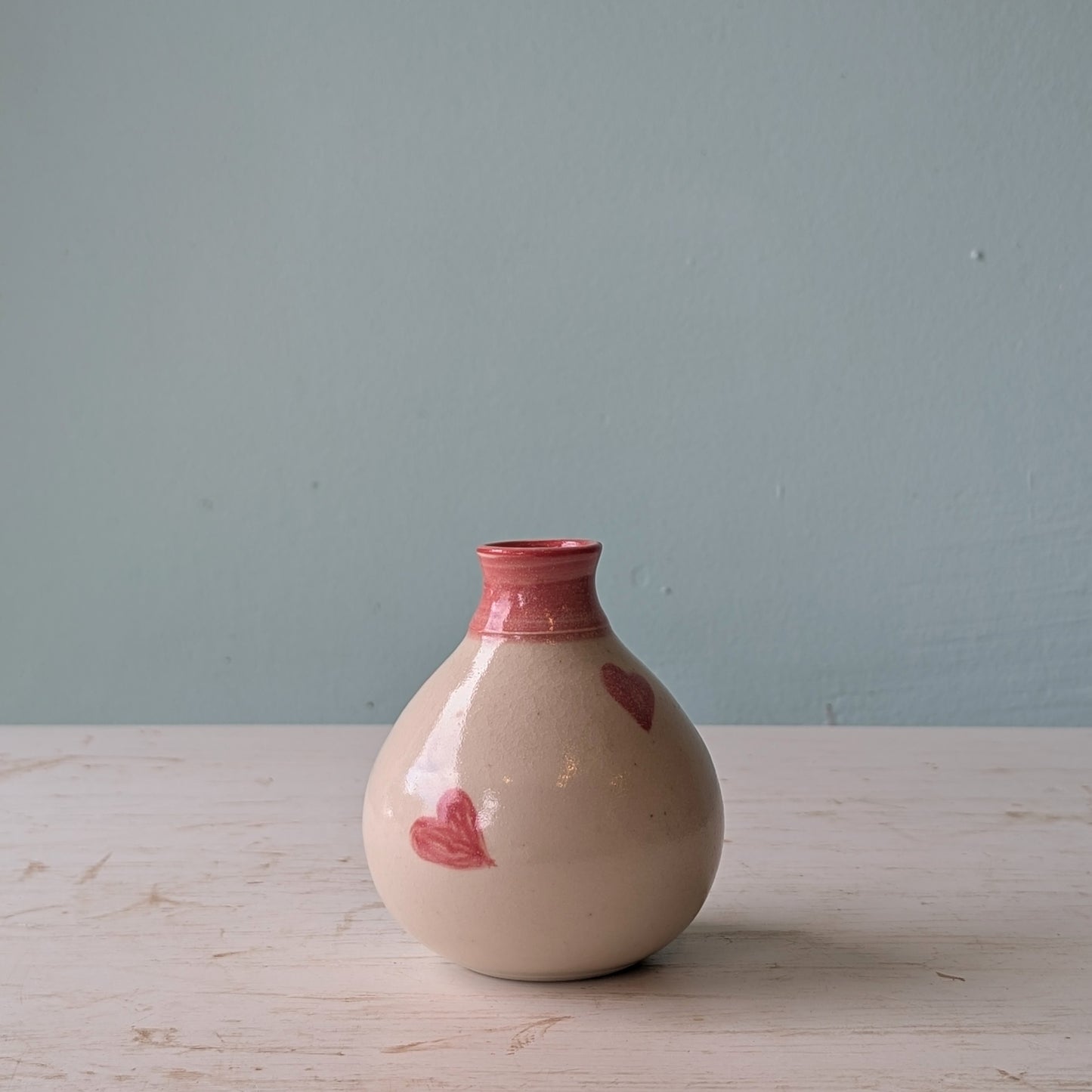 Ceramic vase with pink accents on a light wooden surface and light blue background