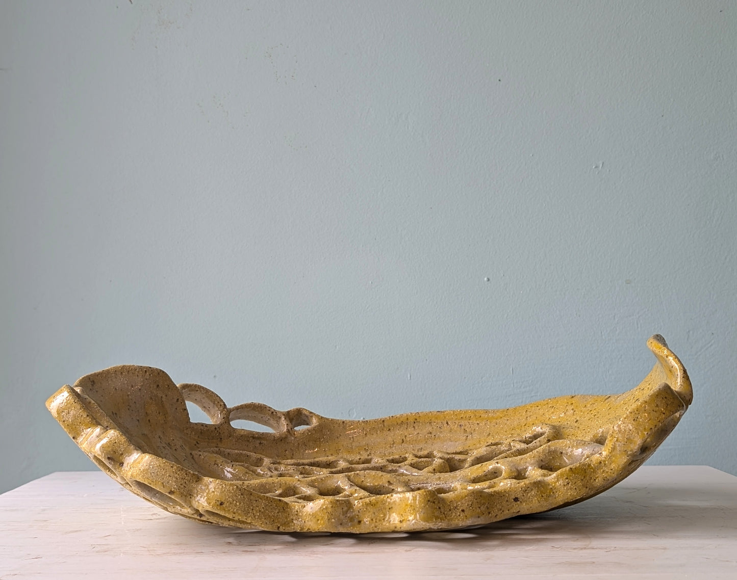Yellow ceramic platter on a white table against a blue wall