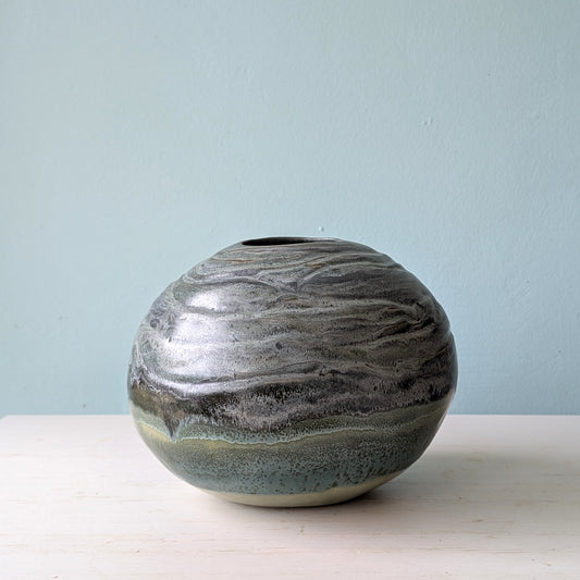 Round blue/green ceramic vase on white table against a blue wall