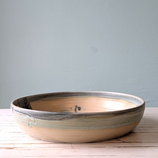 Front view of a blue and green ceramic serving bowl on a white wooden table with a blue background.