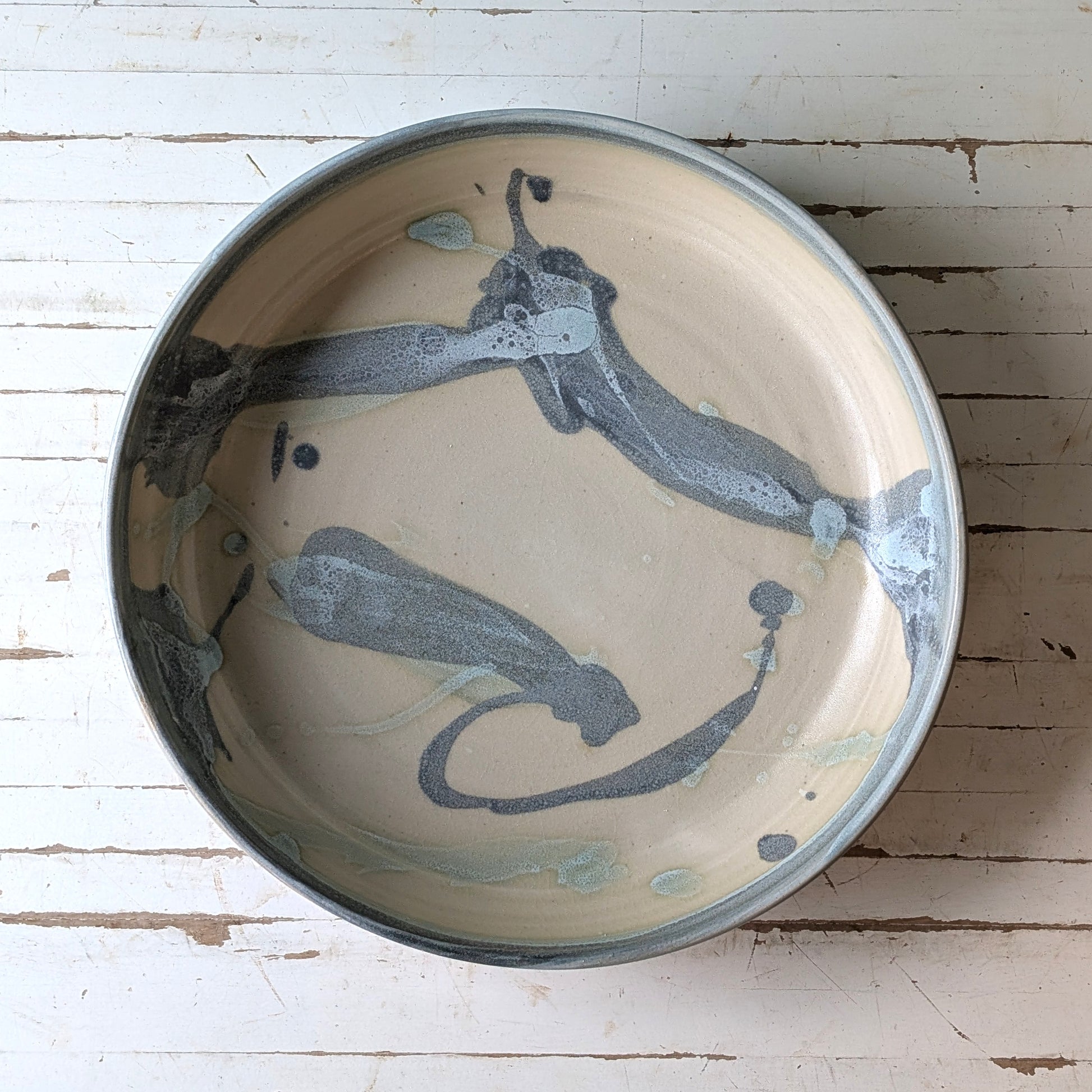 Top  view of a blue and green ceramic serving bowl on a white wooden table.