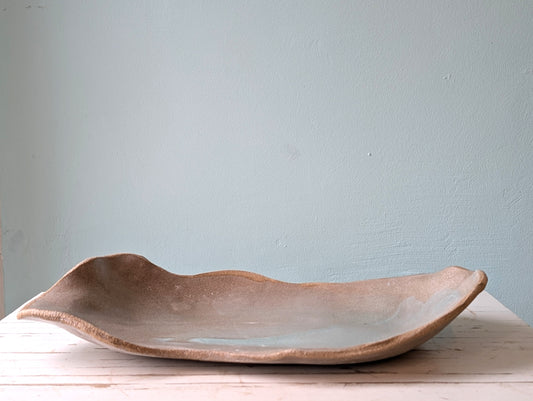 Front view of a freeform ceramic serving platter on a white wooden table with a blue background.
