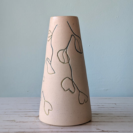 Front view of a beige ceramic vase with carvings of native Australian liana flowers on a white table against a blue background.
