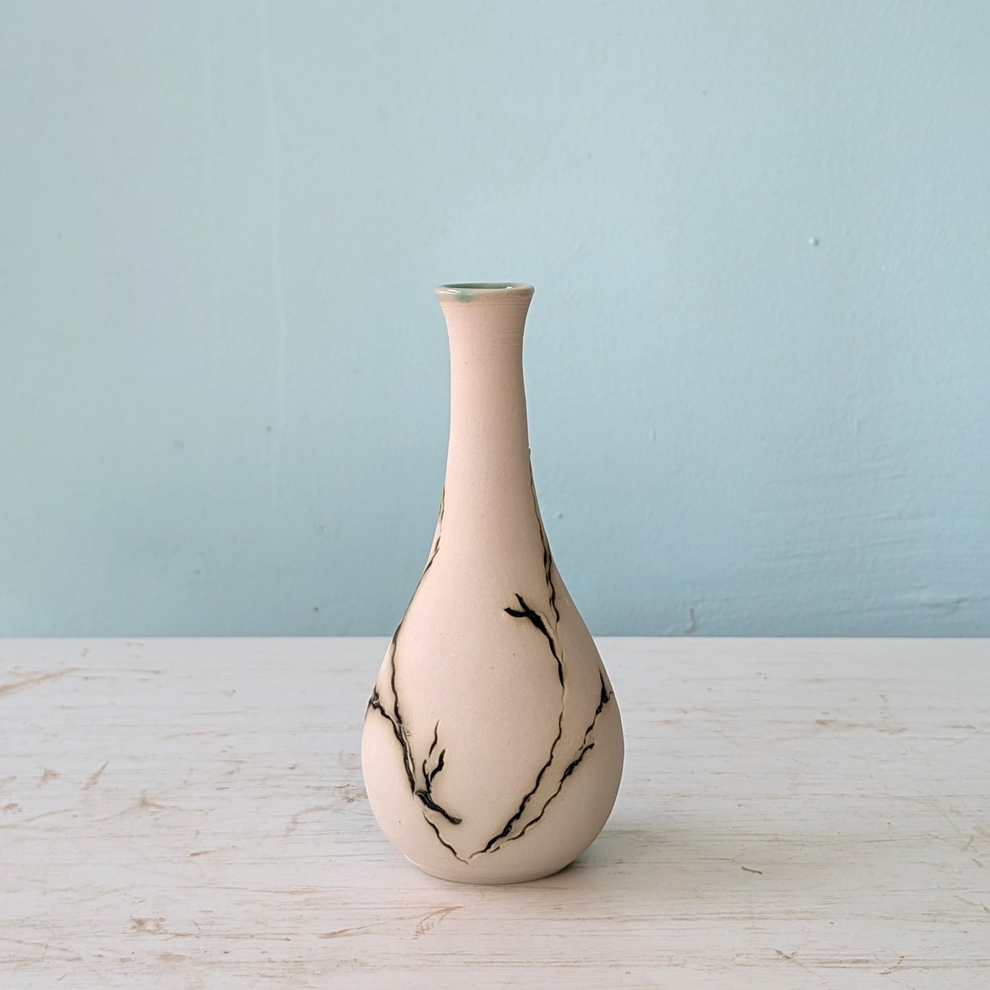 Seagrass-patterned vase on a wooden surface with a light blue background