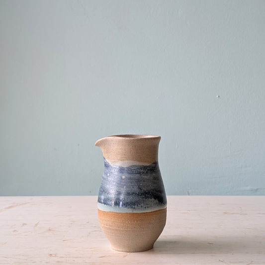 Ceramic pourer with a two-tone design on a light wooden surface and light blue background