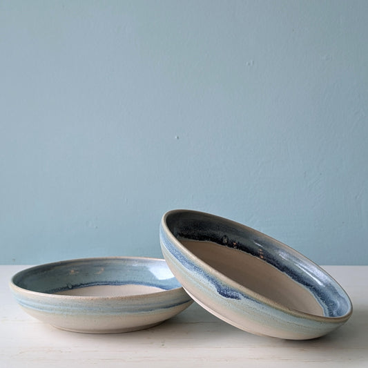 Beige ceramic serving bowls with blue/green edge on white table against a blue wall