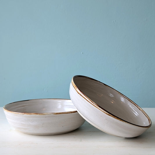 Two white ceramic bowls with brown rims on a light blue background