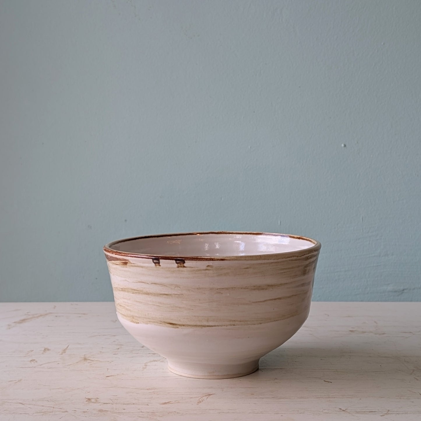 Ceramic bowl with brown rim on a light wooden surface against a light blue wall