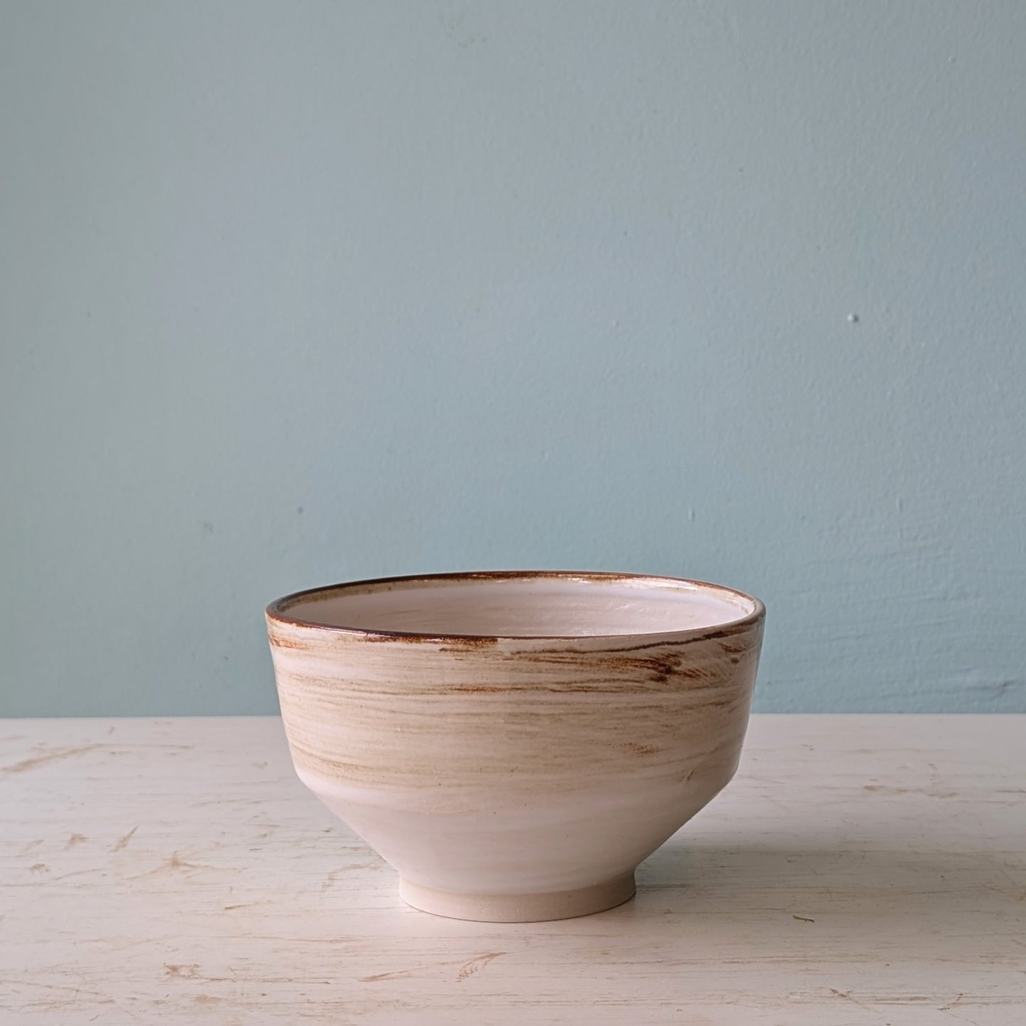 Ceramic bowl with a textured surface on a light wooden table against a light blue wall.