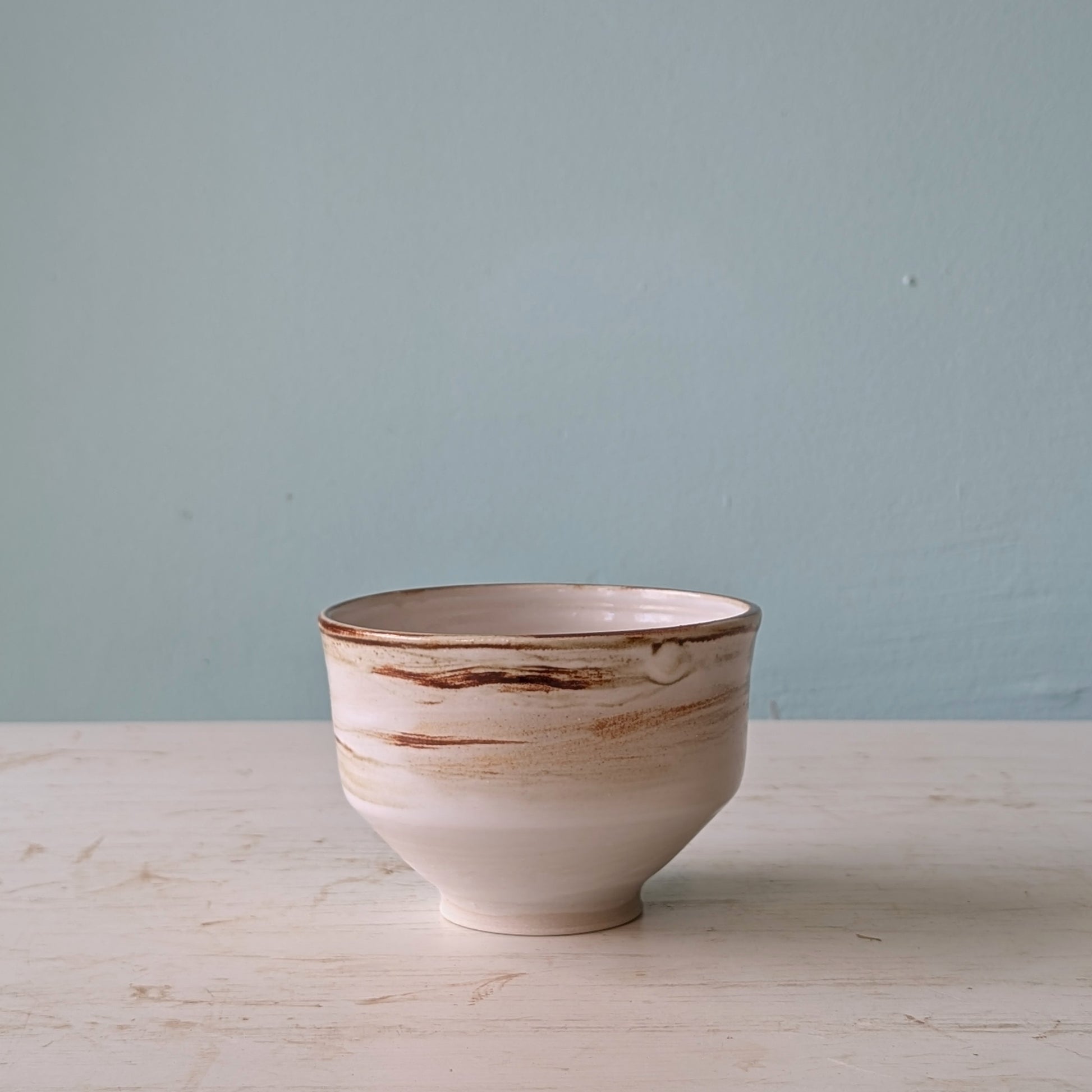 Ceramic bowl with brown accents on a light wooden surface and blue wall background