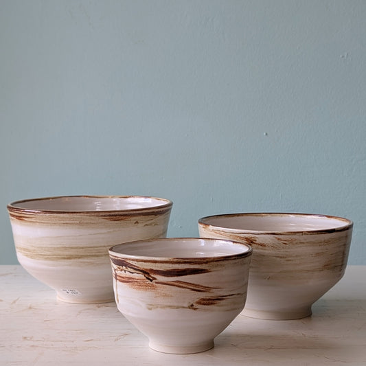 Three ceramic bowls with brown and beige patterns on a light blue background