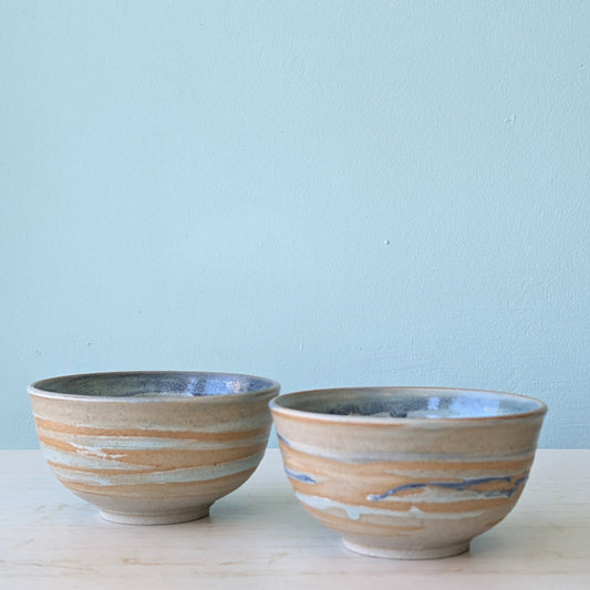 Two beige and blue ceramic bowls on a white table against a blue wall