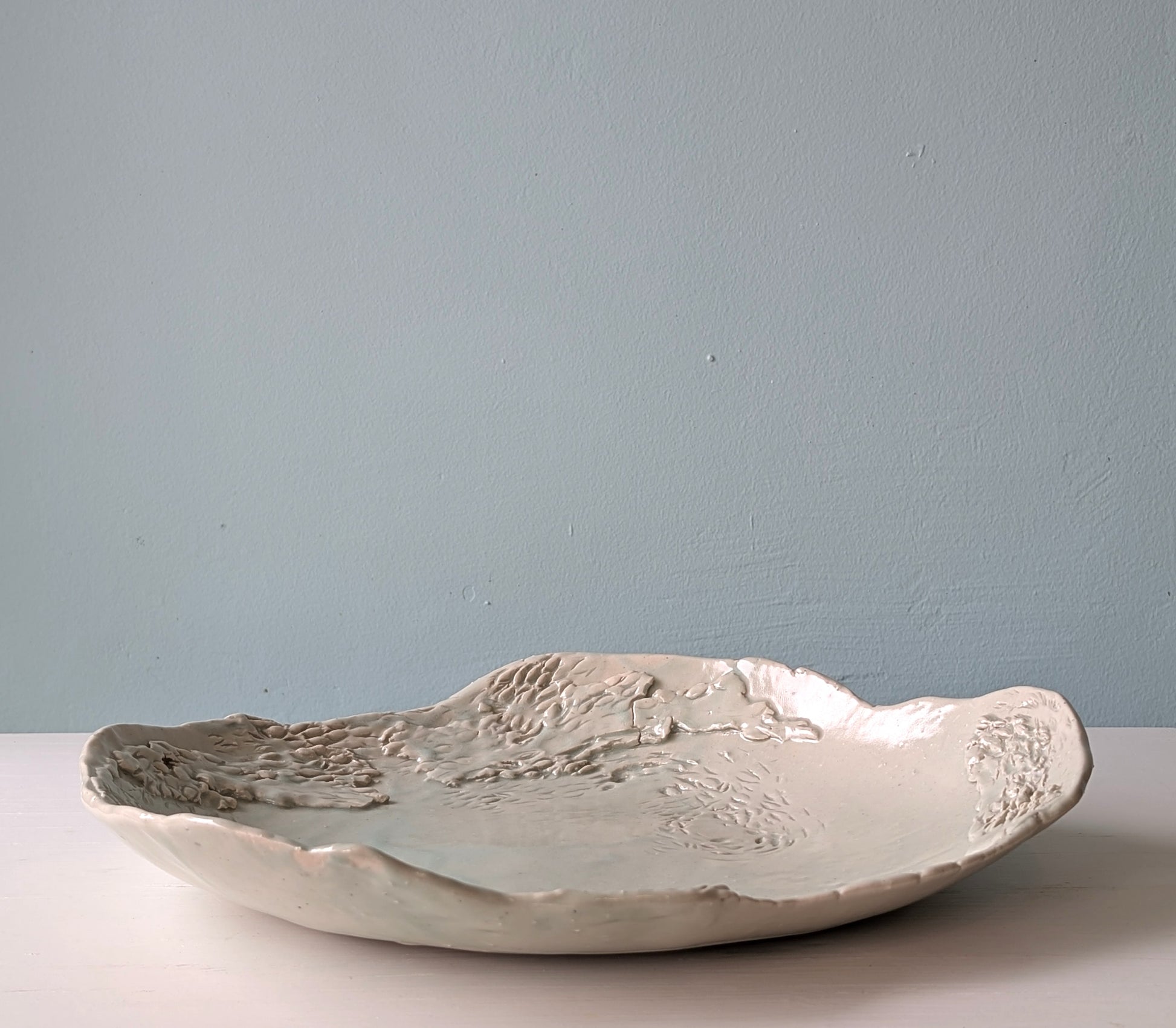 Front view of a green ceramic serving platter with carved and etched detail on white background.