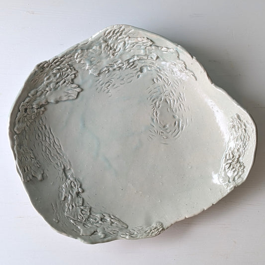Top view of a green ceramic serving platter with carved and etched detail on white background.