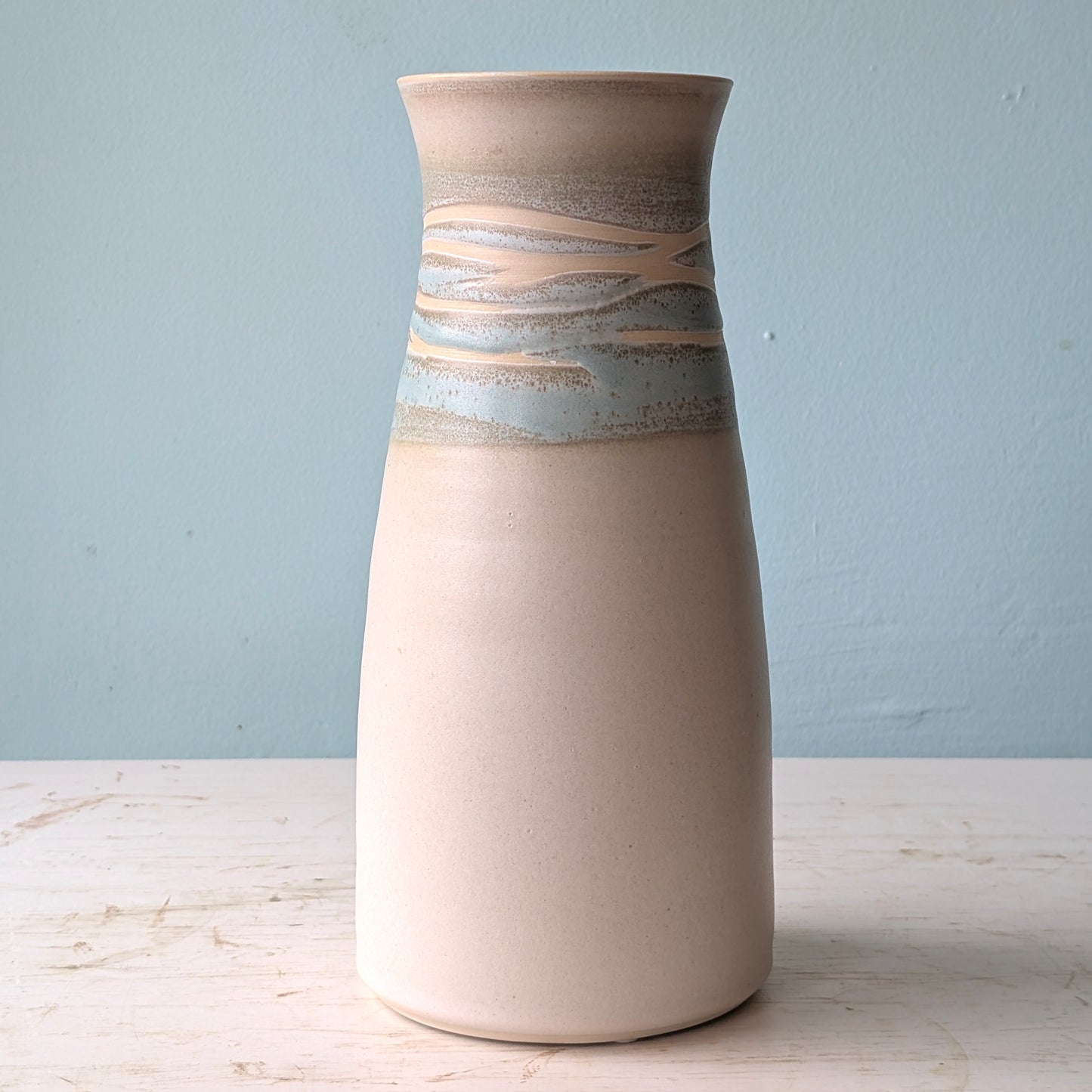 White and green ceramic vase on a white table against a blue wall