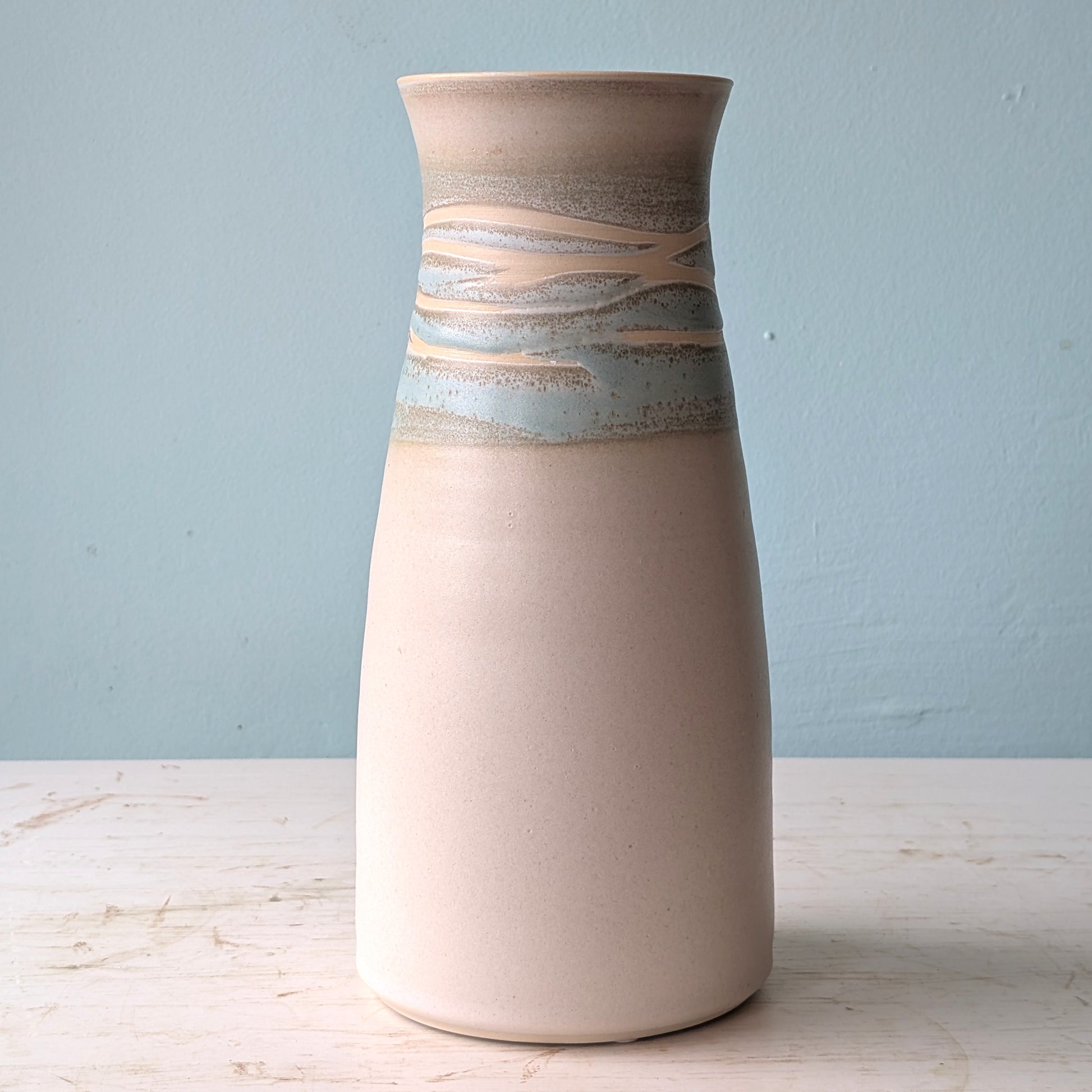 White and green ceramic vase on a white table against a blue wall