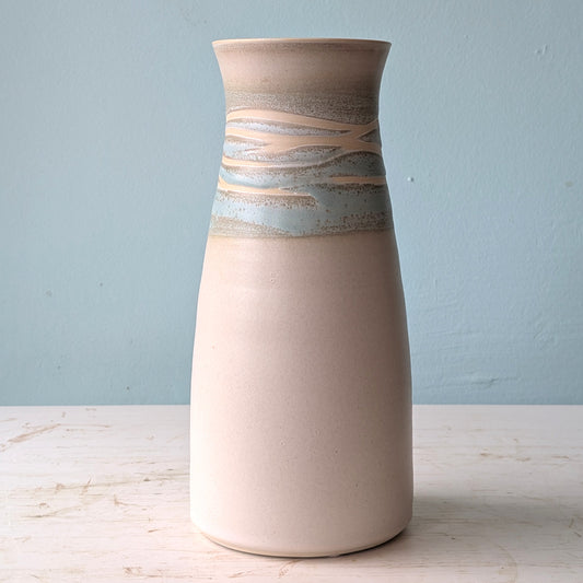 White and green ceramic vase on a white table against a blue wall
