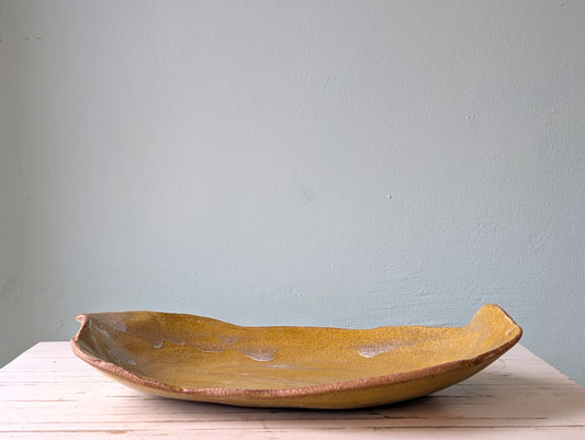 Front view of a freeform yellow ceramic platter on a white wooden table with a blue background.