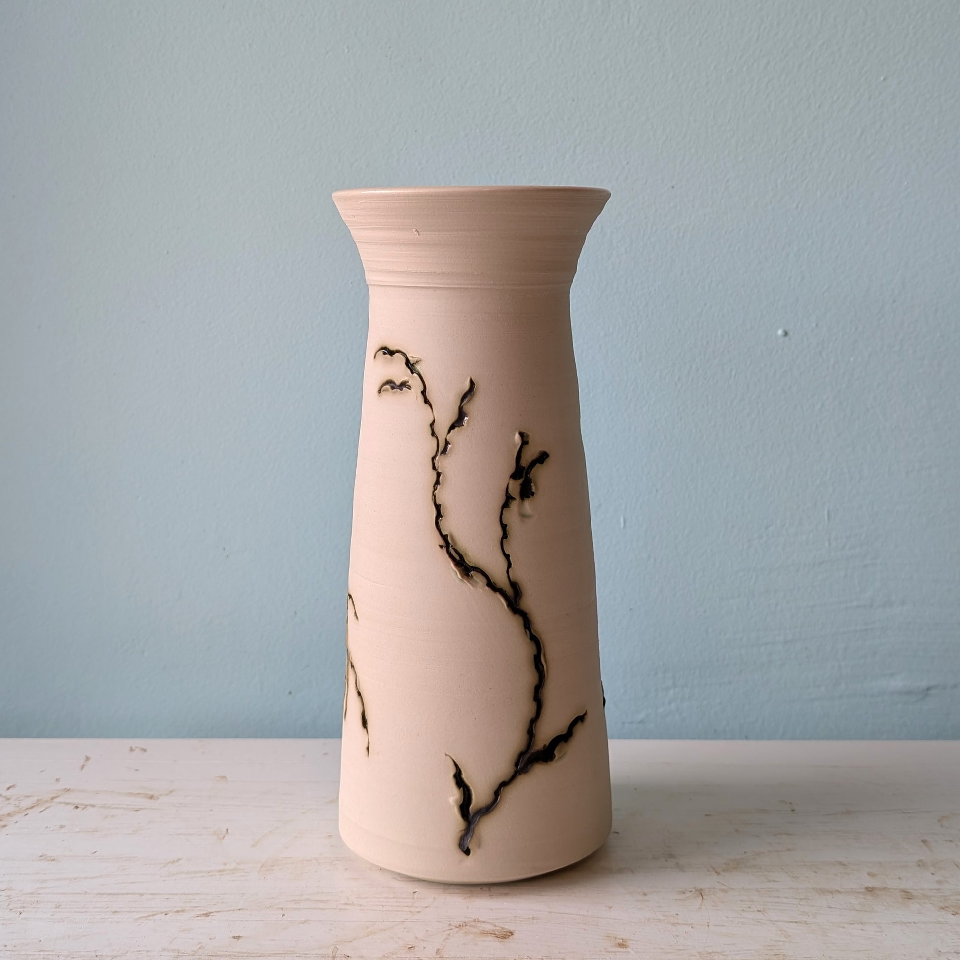 Ceramic vase with green seagrass pattern on a white table against a blue wall.
