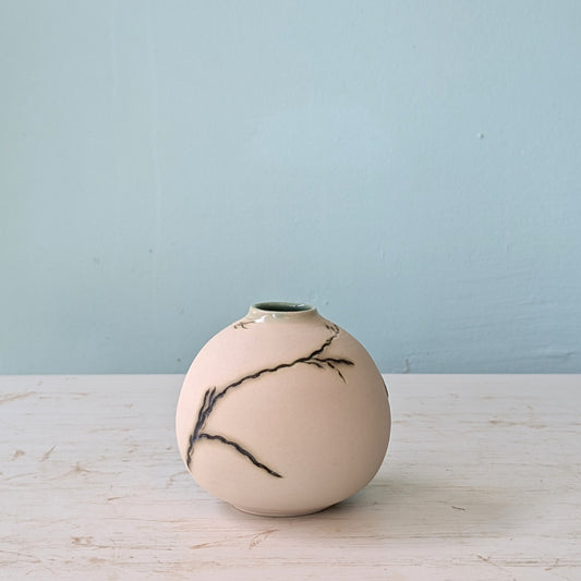 Beige ceramic vase with green seagrass design on a light wooden surface with a light blue wall background