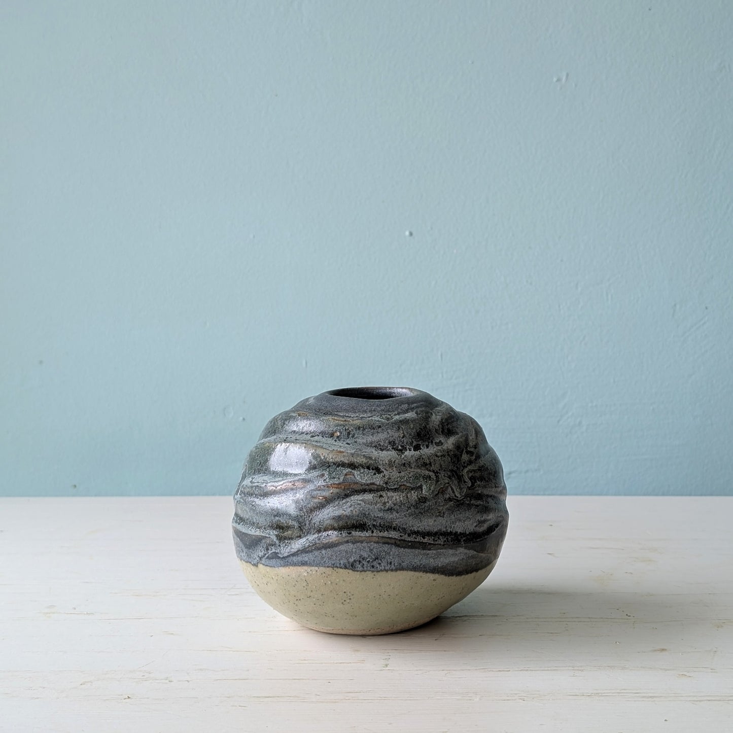 Blue/green round ceramic vase on white table against a blue background