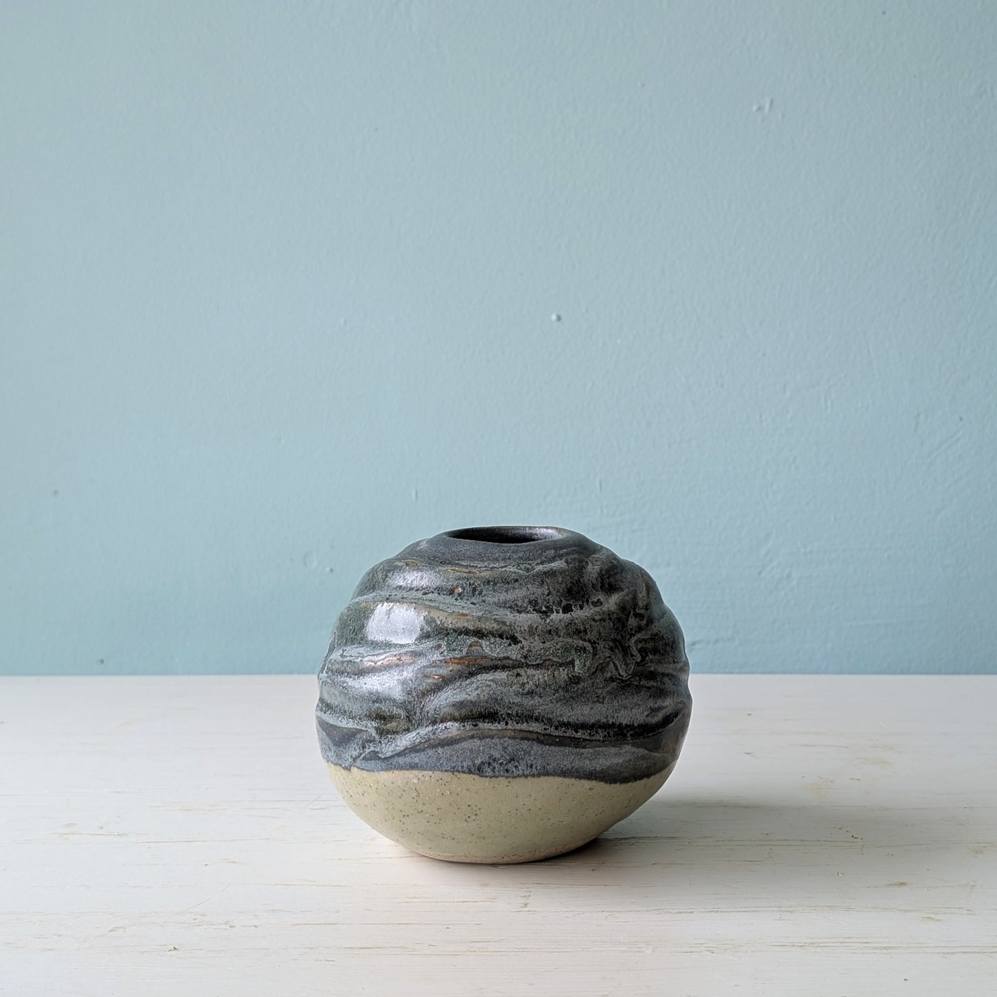 Blue/green round ceramic vase on white table against a blue background