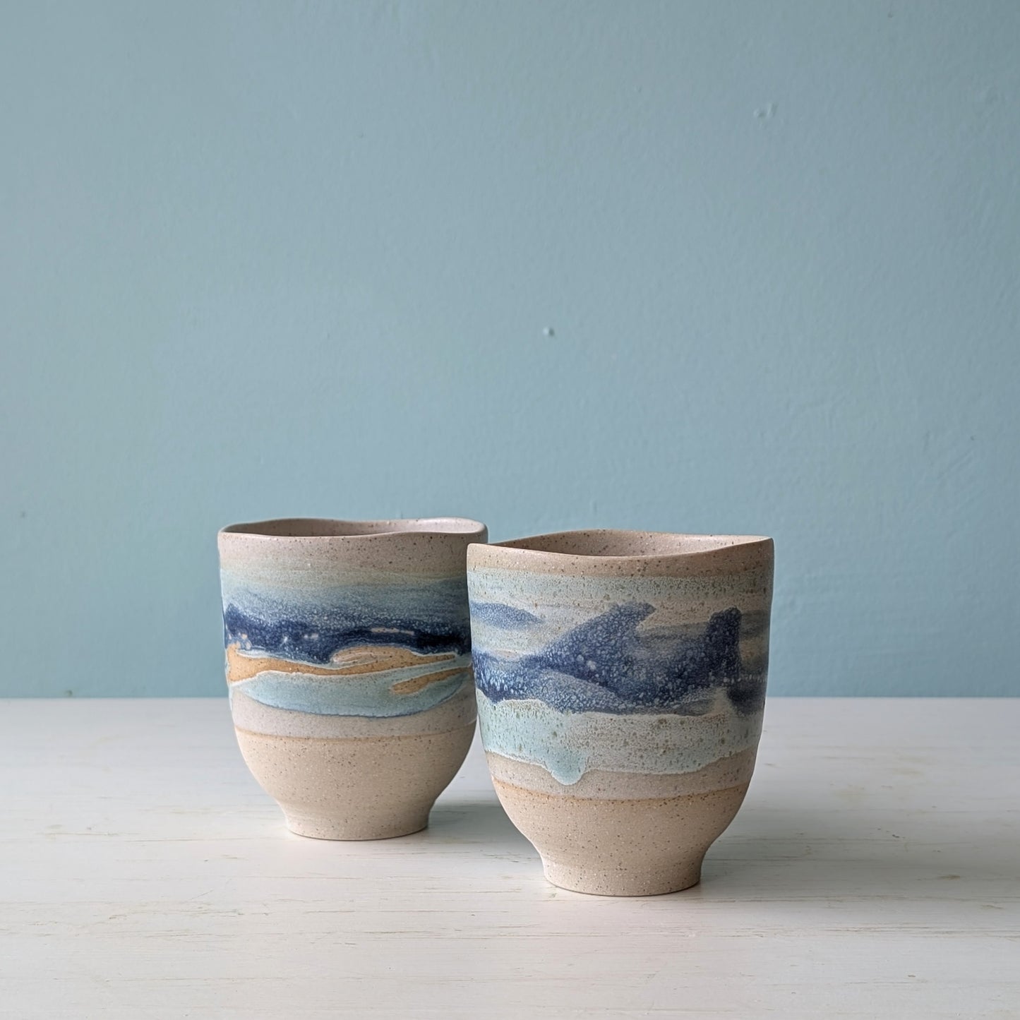 Two beige ceramic cups with dark blue glaze