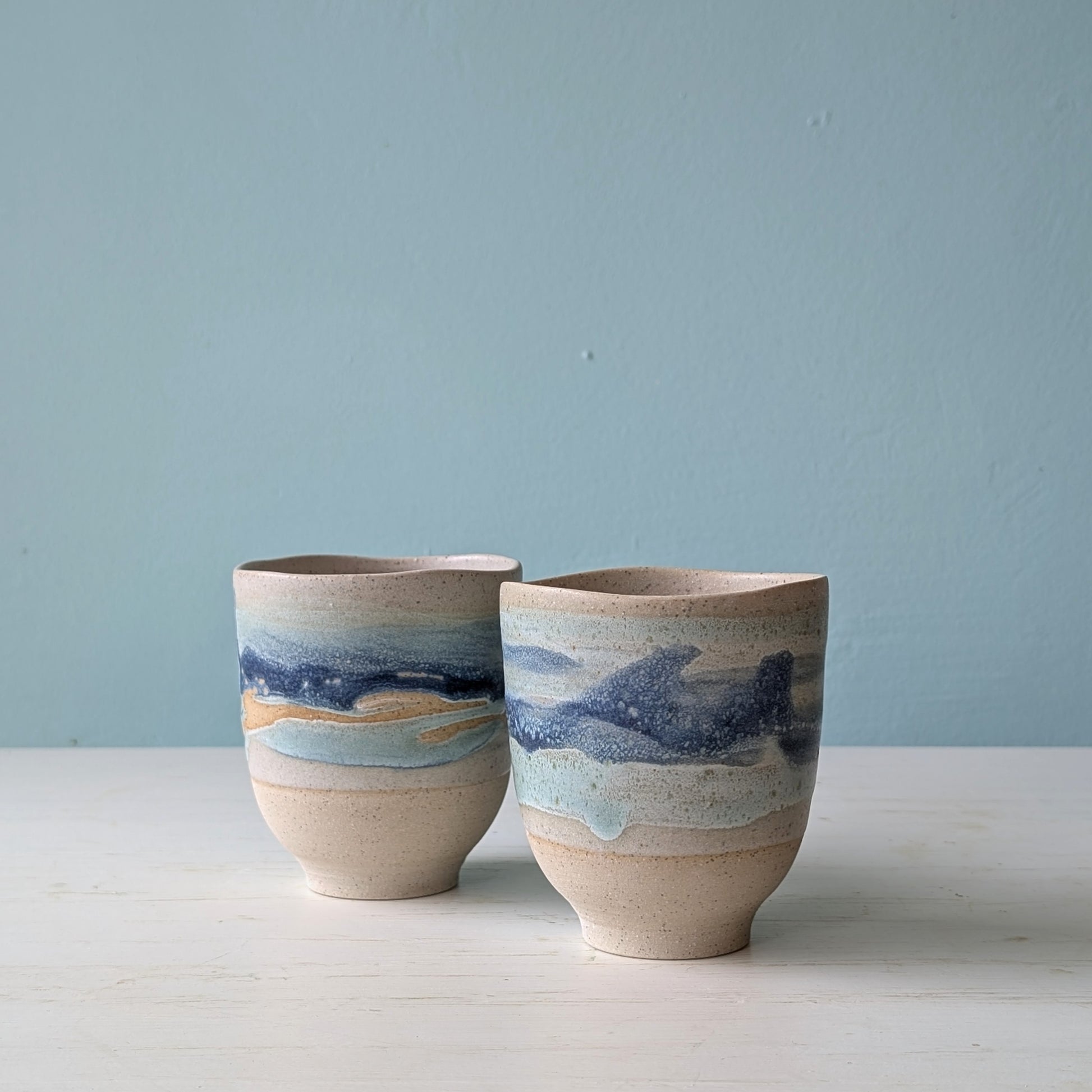 Two beige ceramic cups with dark blue glaze