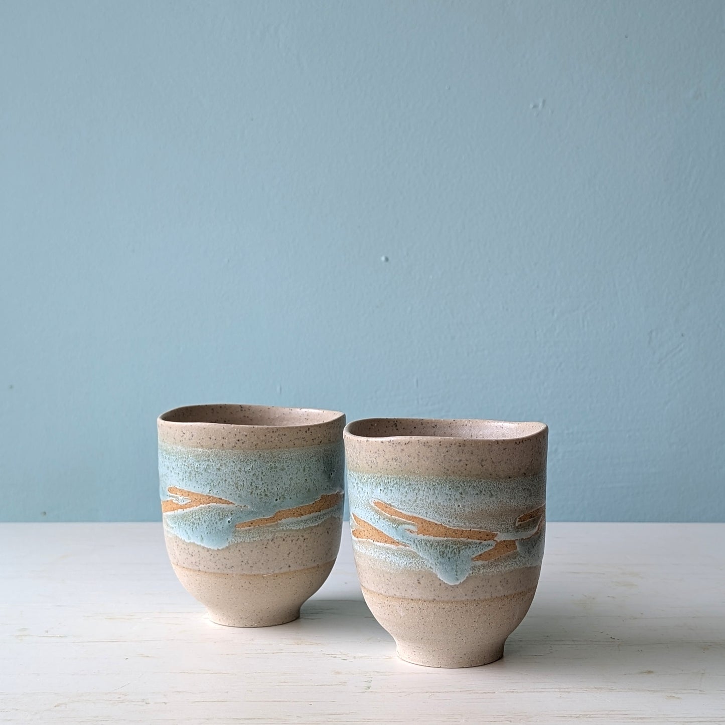 Two ceramic cups with striped design on a light blue background