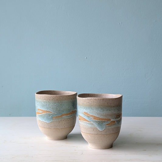 Two ceramic cups with striped design on a light blue background