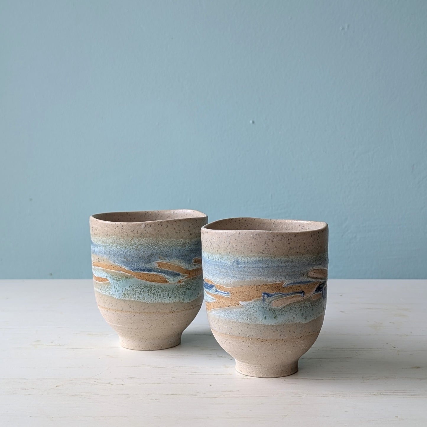 Two beige ceramic cups with light blue glaze